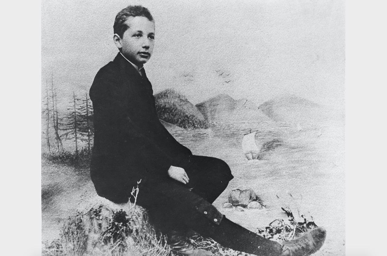 A young Albert Einstein sits on a rock in the country.
