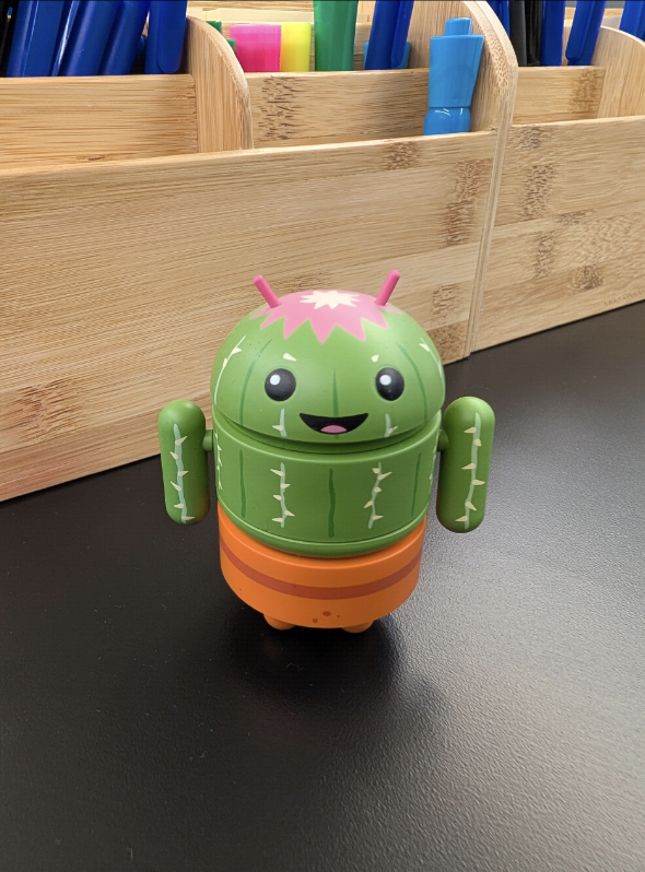 A small, green Android robot with a cactus-like design sits on
             a black surface.
