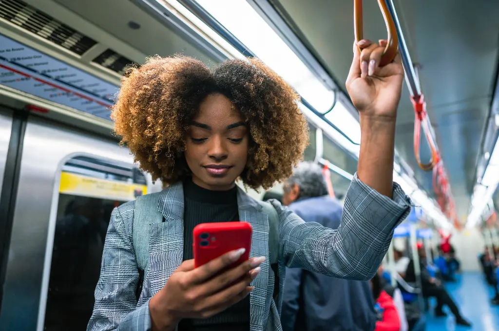 Linha metrô - Mulher negra de cabelos cacheados usando um celular enquanto viaja no metrô.