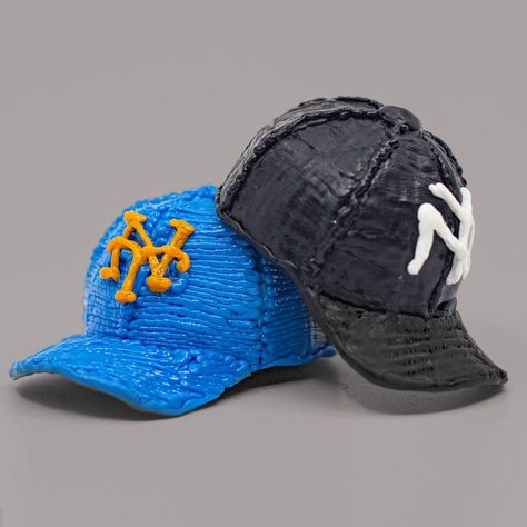 two baseball caps are sitting side by side on a gray surface, one is blue and the other is black