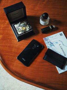 a wooden table topped with a cell phone next to an empty wallet and other items