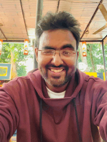 a man wearing glasses and a maroon hoodie smiles