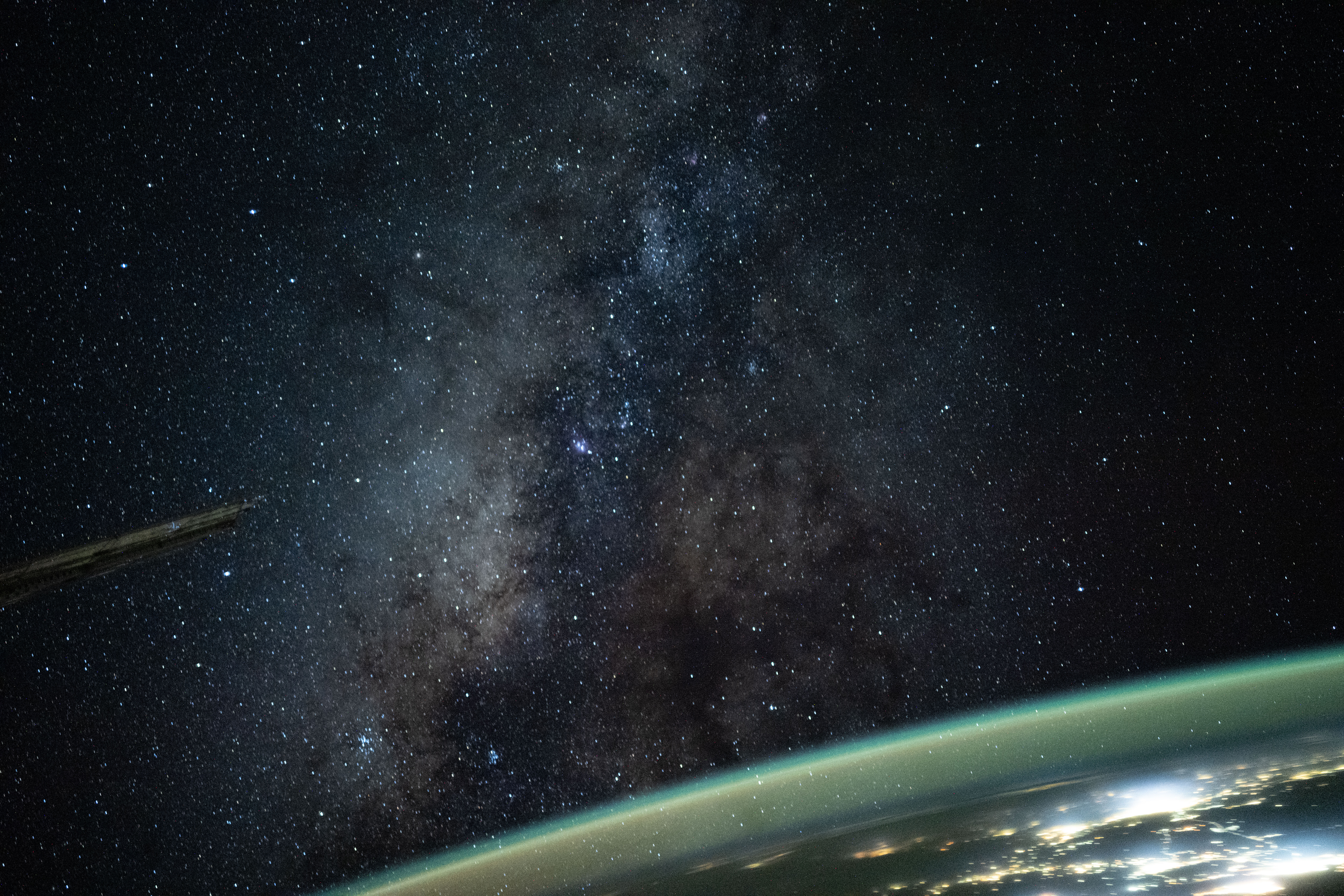 The Milky Way galaxy appears above Earth's greenish atmospheric glow. The galaxy's dust and stars can be seen against the darkness of space.